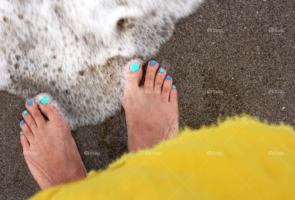 Bare feet on the sandy beach, wave coming