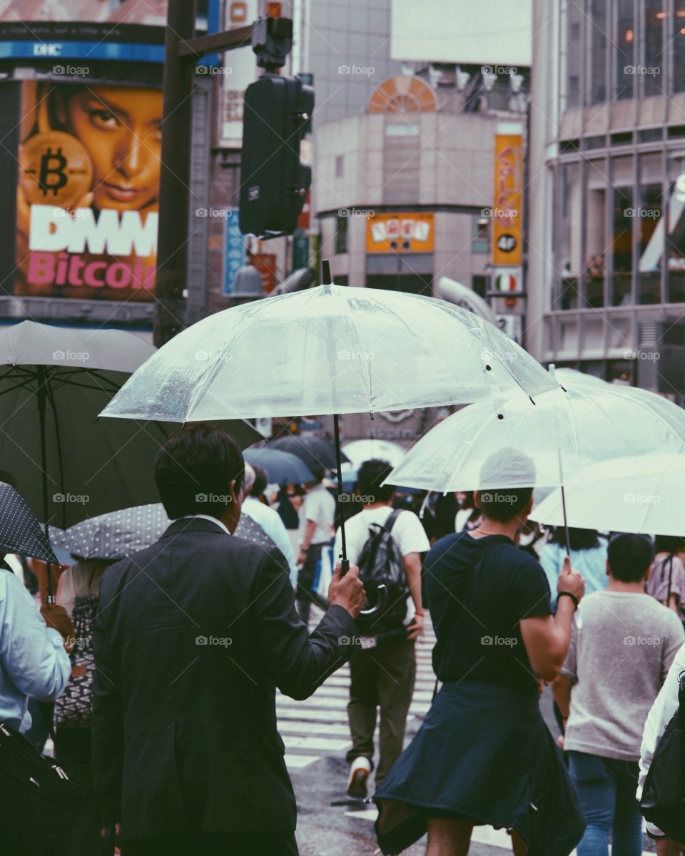 Pedestrians with umbrellas on a dark, rainy day at Shibuya Scramble crossing. 