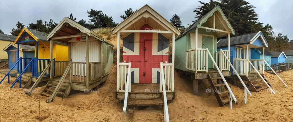 A row of colourful beach huts on the sandy beach at Wells-next-the-Sea in Norfolk, UK with a patriotic, painted on Union Jack flag 