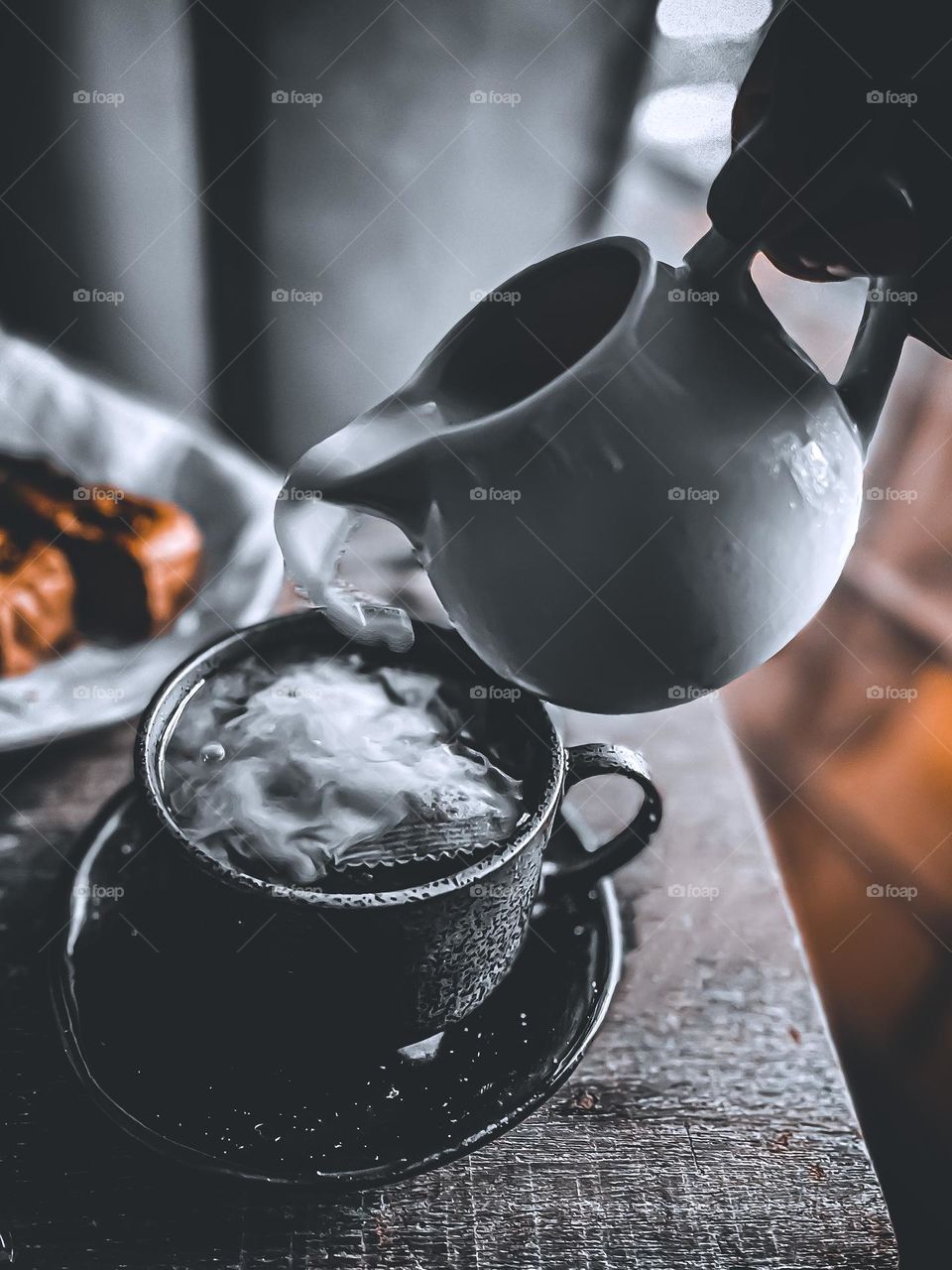 Pouring milk into a cup of hot black coffee in close up view