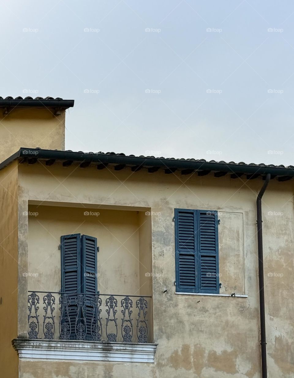 Old beige building, door and window with bluish and greenish shutters on the background of clear sky, Italy, Ravena 