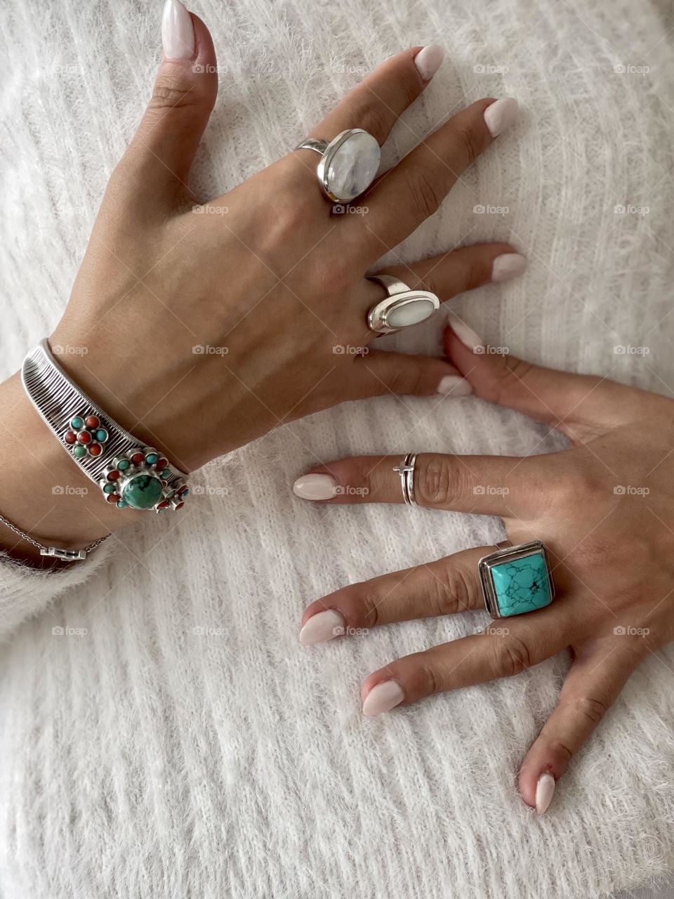 Woman’s hands wearing white nail polish manicure, silver and semi precious stones rings and bracelets 