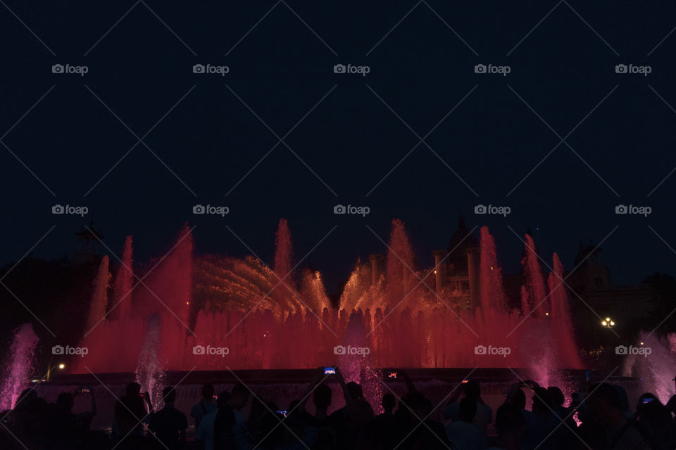 The magic fountain show in Barcelona. The square is full of columns, fountains and stairs, with a beautiful museum behind it. At night everything is framed by the show.