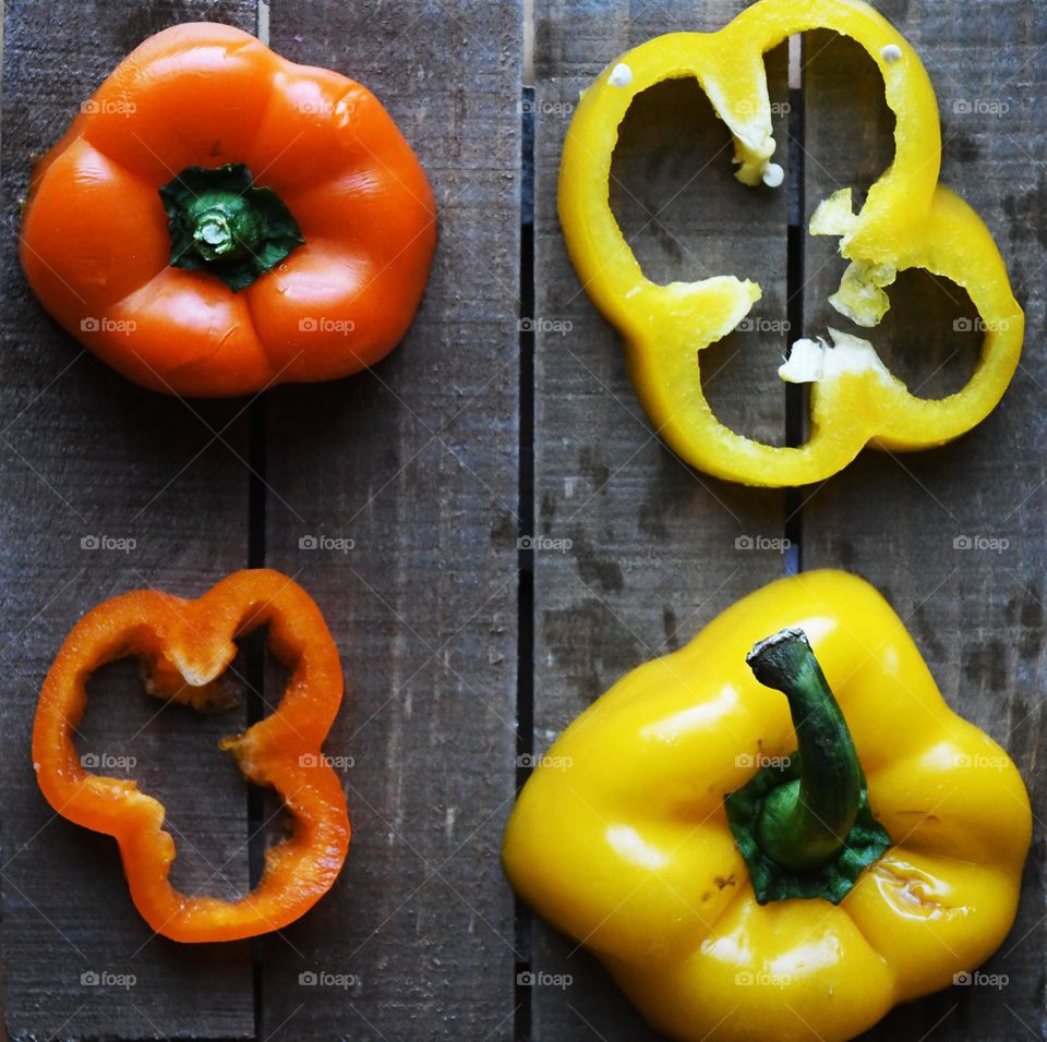A yellow and orange pepper are sliced in equal parts in the flat lay point of view on a wooden cutting board.
