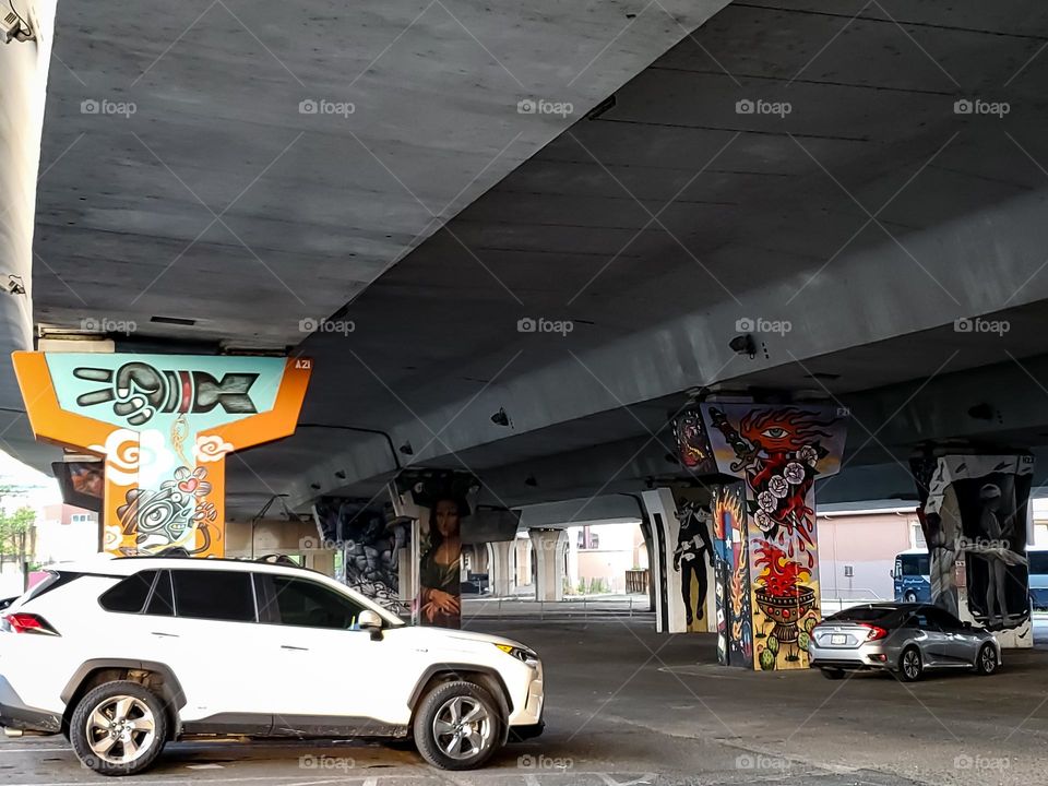 City parking under highway with street art on the highway pillars.