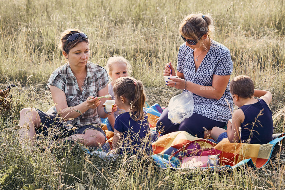 Families and friends spending time together on a meadow, close to nature. Mothers feeding kids, sitting on a blanket, on grass. Candid people, real moments, authentic situations