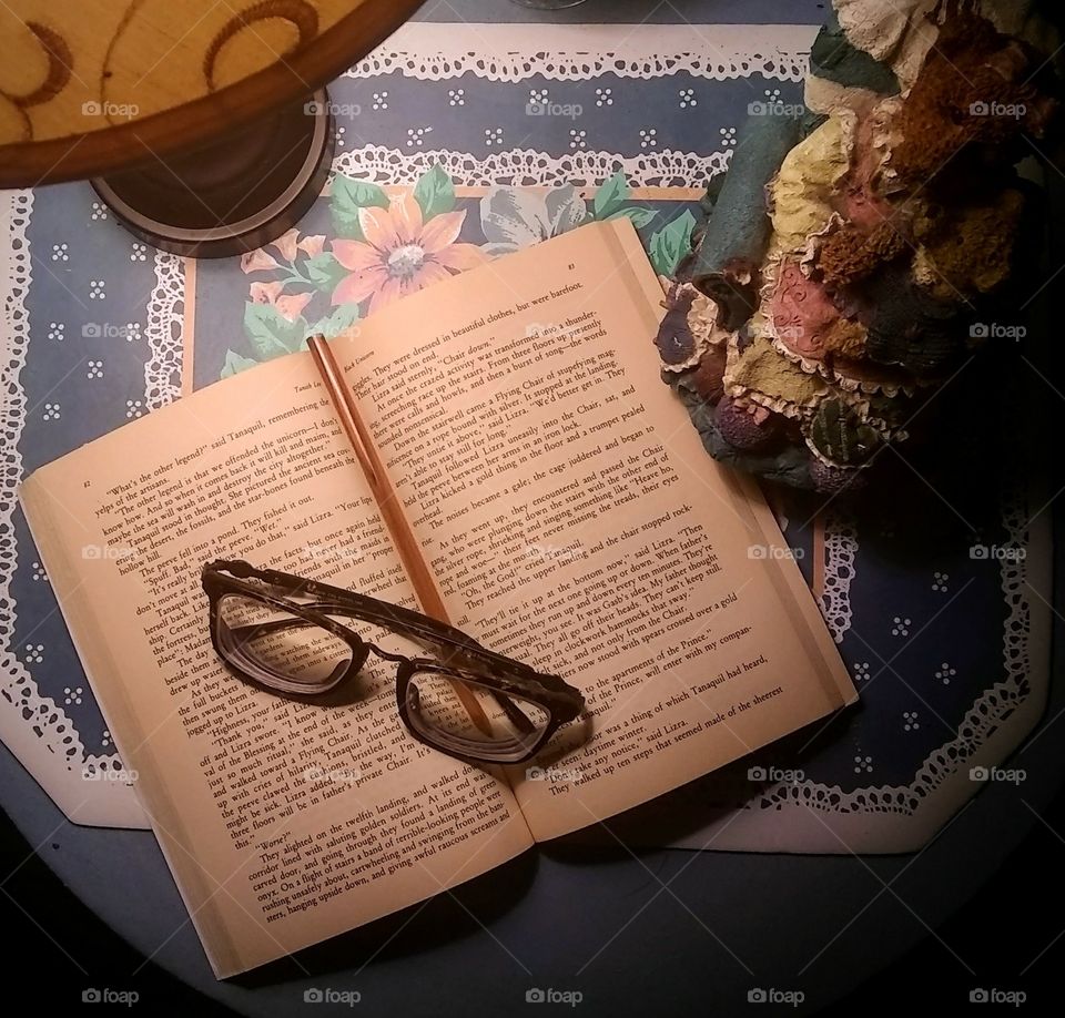 Book and glasses on a bedside table under lamp light