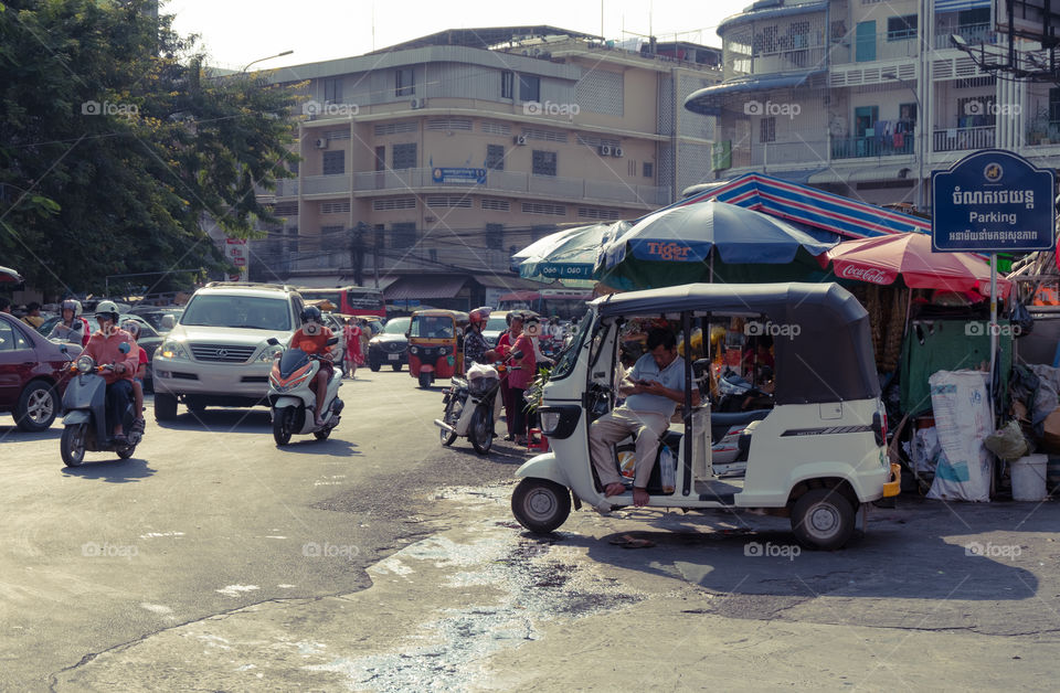 People traveling around the market and man sitting on tuk tuk