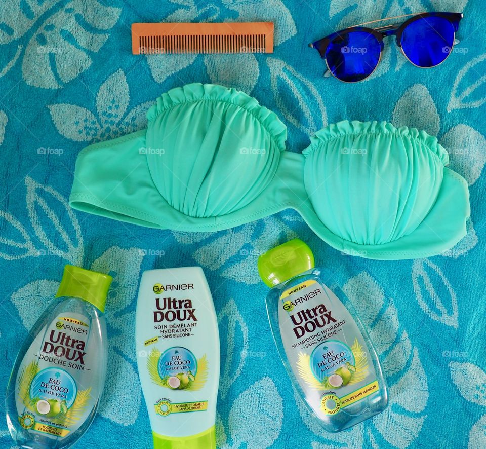 Garnier eau de coco shampoo, conditioner and bath gel on a blue towel with comb and bikini.