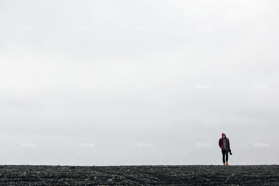 Man walking in hoodie over black sand. Minimalist man walking with camera over a black sand beach in Iceland