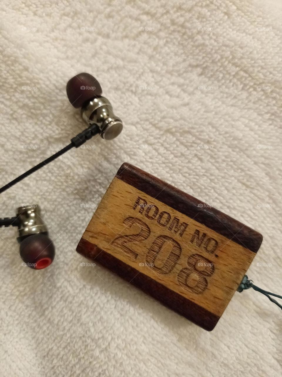 Closeup photo of engraved Hotel room nomber keychain with 208 nomber nice background of what colour and earphone