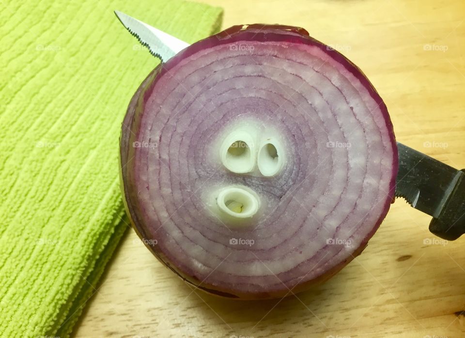 A red onion that looks like a shocked face being sliced by a knife on a counter top in the kitchen.