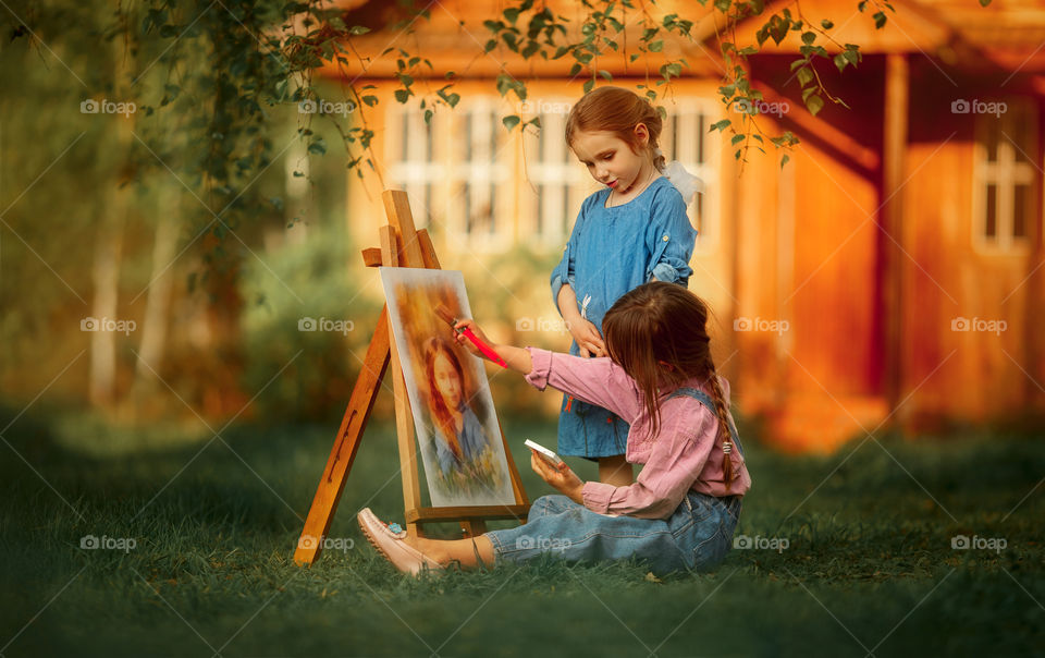 Little girl painting her sister at sunset