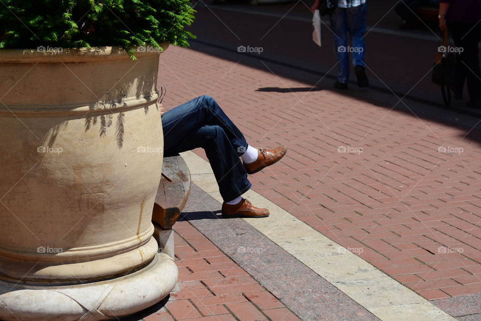 Man  with crossed legs. Male is siting in the park. White socks and brown-yellow shoes