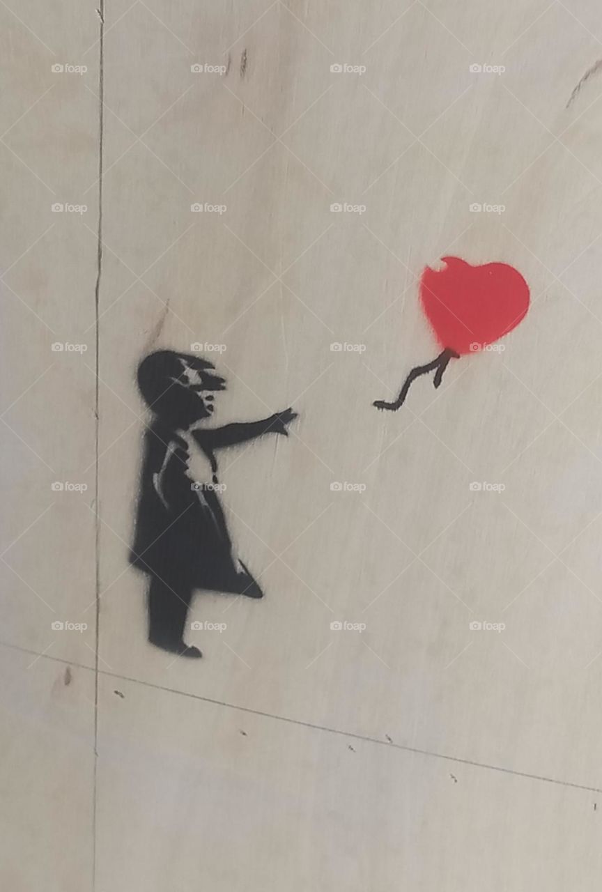 A stencil made on the wall of a Banksy exhibition represents the drawing of a little girl who lets out a red balloon. This exposition takes place in Brest, France, on June 2023.