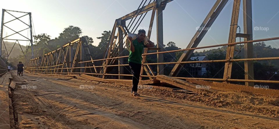 A man within a sunset light and an village bridge