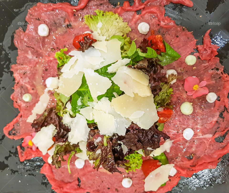 Carppaccio salad on the plate with meat, vegetables and cheese.