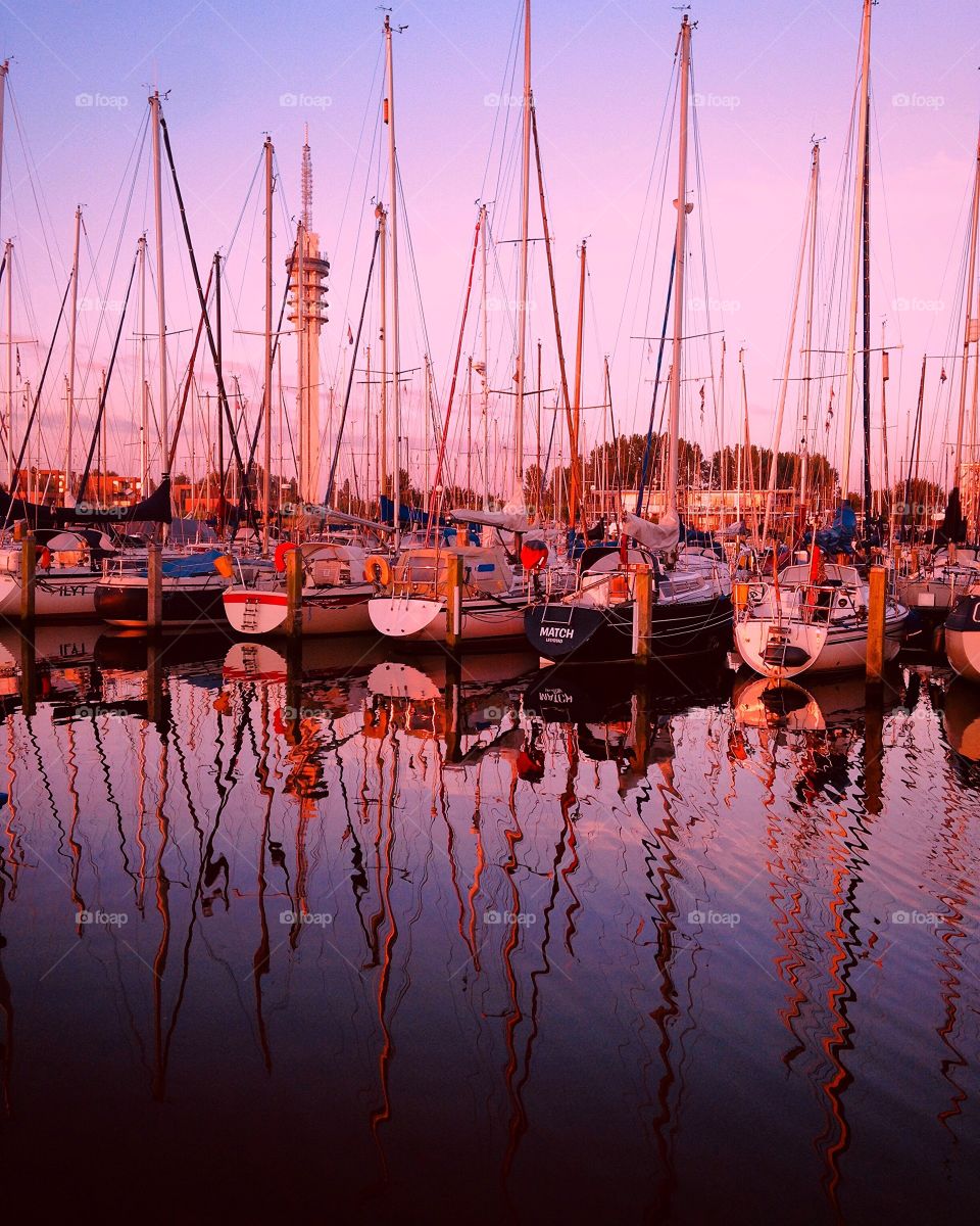 late afternoon at a marina with reflections of sailboats in the sea