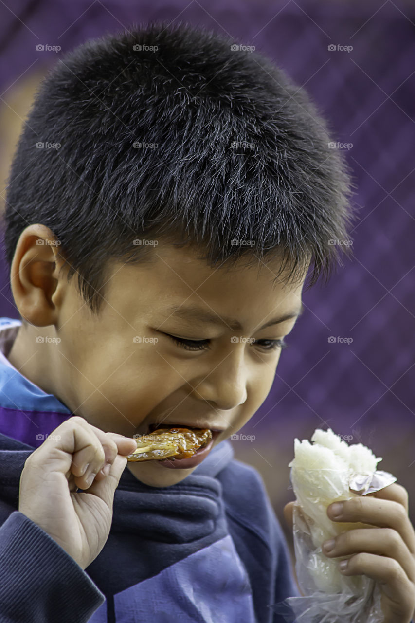 Asian boys are eating sticky rice and pork roast , The food is simple and popular to eat breakfast in Thailand.