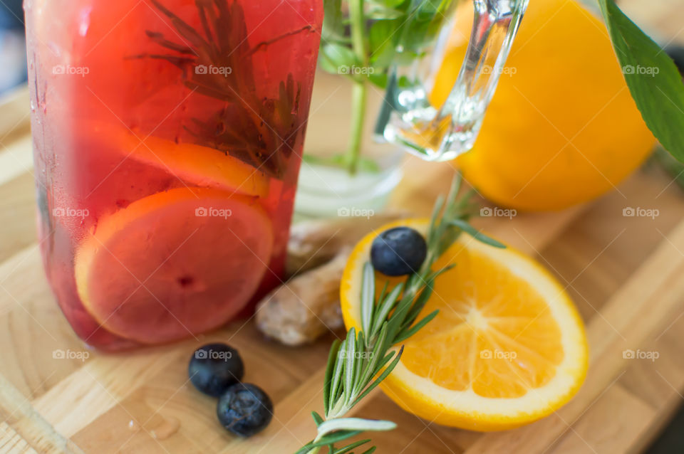 Beautiful summer drinks Aromatic and healthy juice on dark wood tray with ingredients for wellbeing and healing are ginger root, antioxidant blueberry, aromatic rosemary herb and vitamin rich sliced orange 