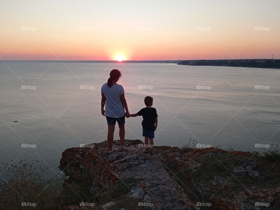 Mom and kid at sunset over the sea