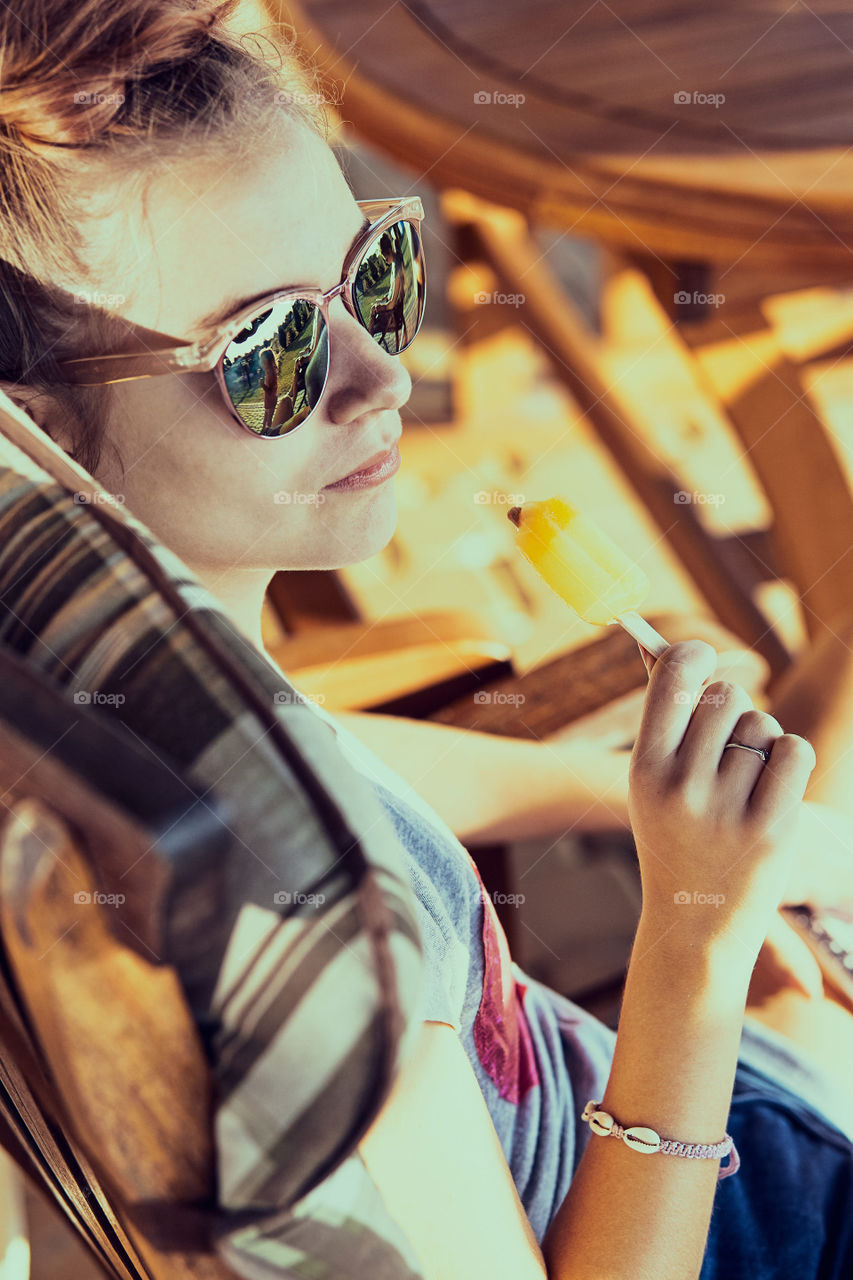 Young woman eating a ice cream, sitting in a chair outdoors on a patio during summer day. Real people, authentic situations