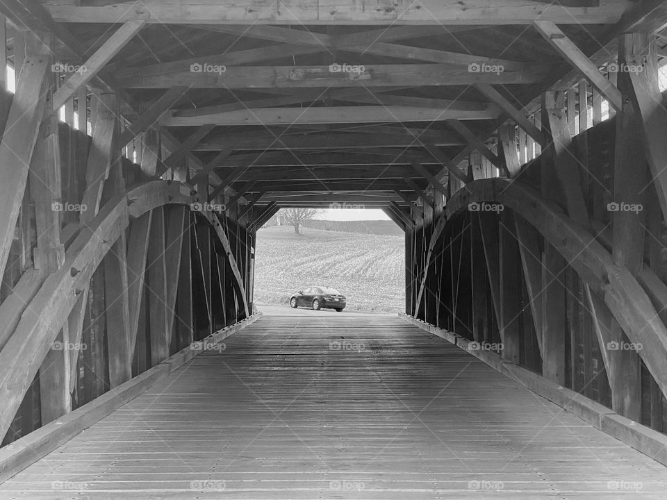 A covered bridge with a car and cornfields in the distance