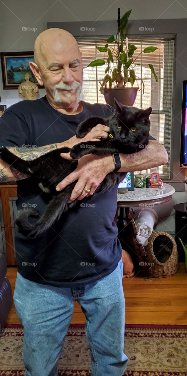 Black cat being held in arms of a man who makes her feel safe and loved.  Pic of trust between a man and a cat🐾