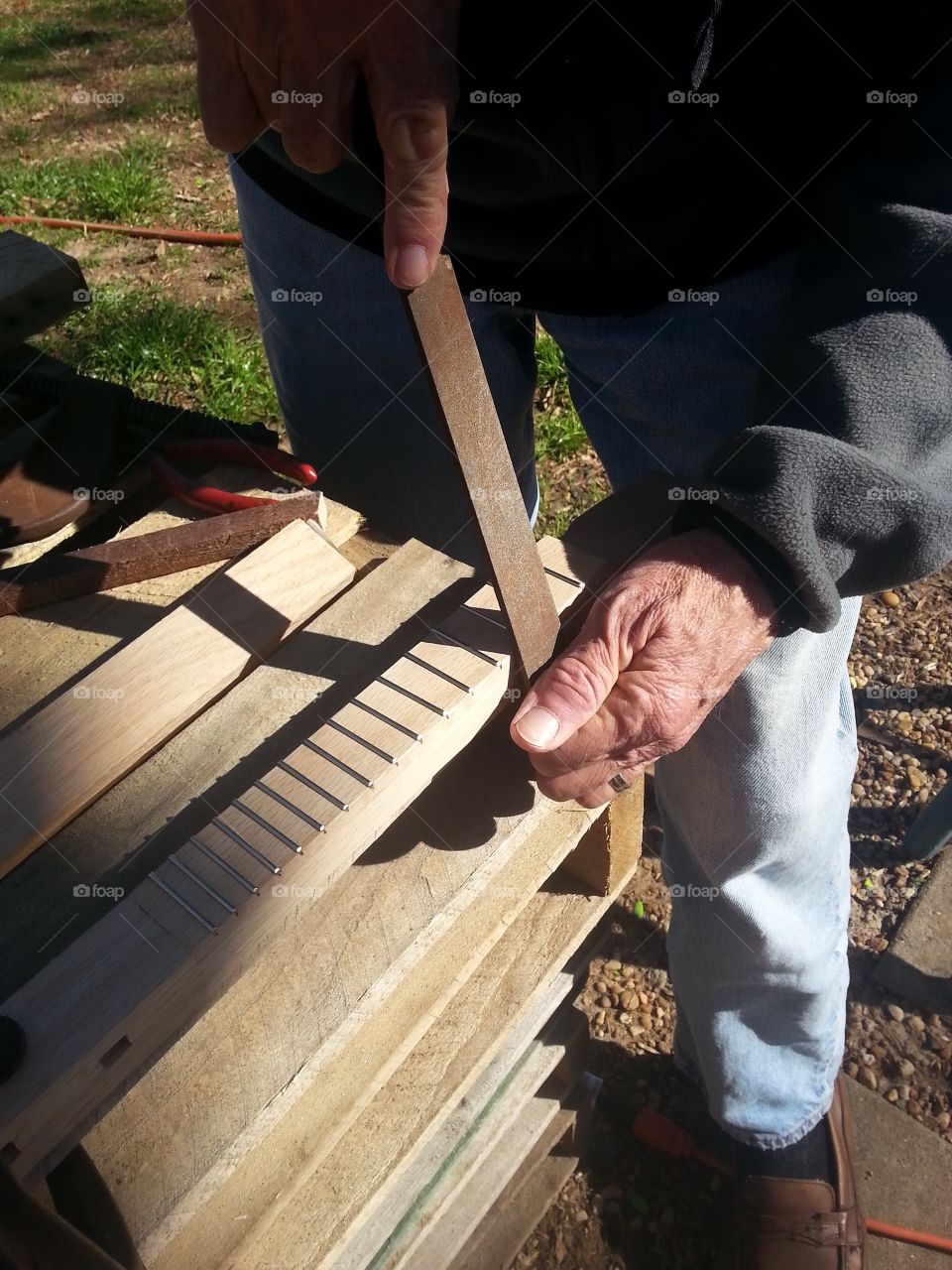 Man filing off the edges of the frets on a guitar neck for the guitar he is making.