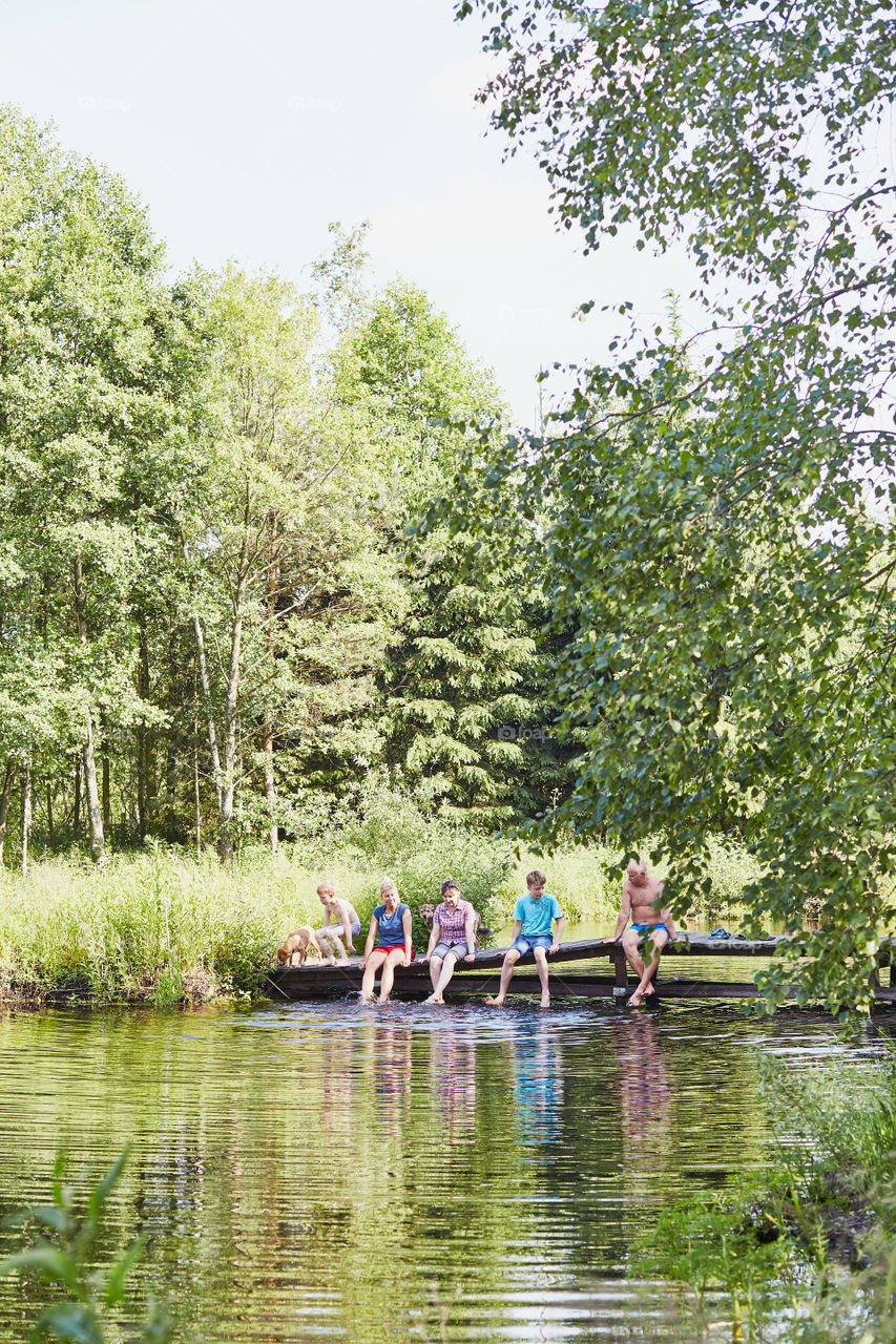 Family spending time together sitting on a bridge over a lake, among the trees, close to nature, during summer vacations. Candid people, real moments, authentic situations