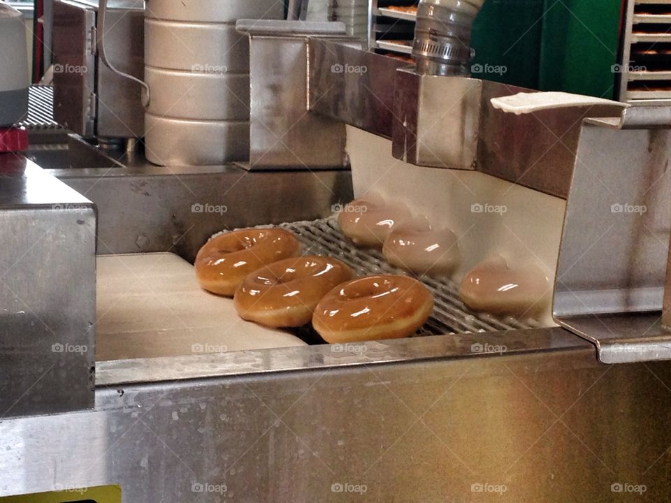 Covered in sweetness. Donuts being glazed on conveyer at Krispy Kreme 