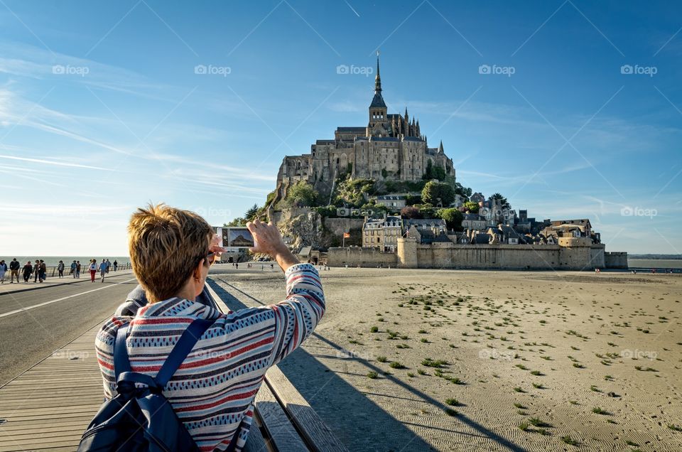 Woman takes a photo of Mont Saint Michel with her smartphone 