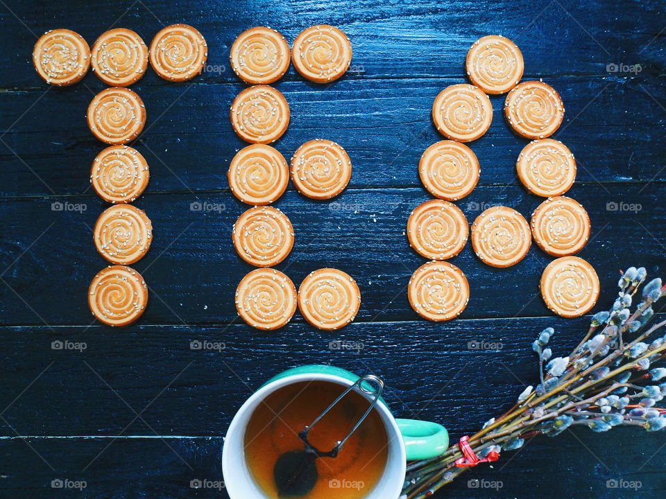 cookies, a cup of tea and willow branches on a black background