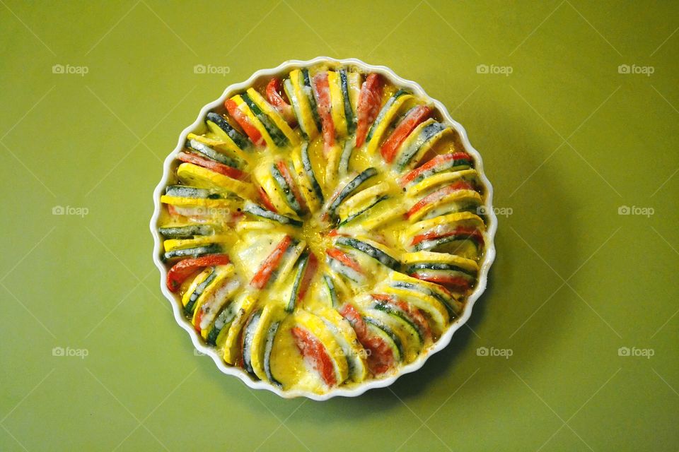 Vegetable Tian of sliced zucchini, tomatoes, potatoes and yellow or summer squash smothered in cheese on a bed of onions and garlic roasted in a round casserole dish is delicious