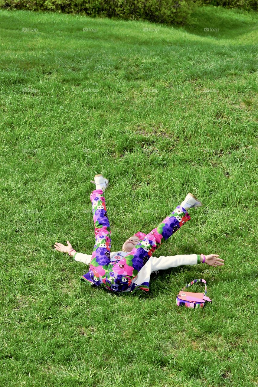 Little girl in colorful clothes lies on green grass