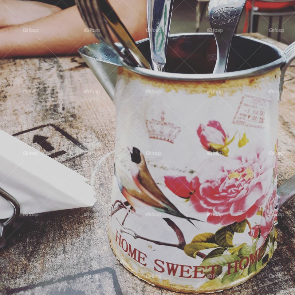 Close-up of a beautifully decorated watering can  used for keeping cutlery on a table in a pub