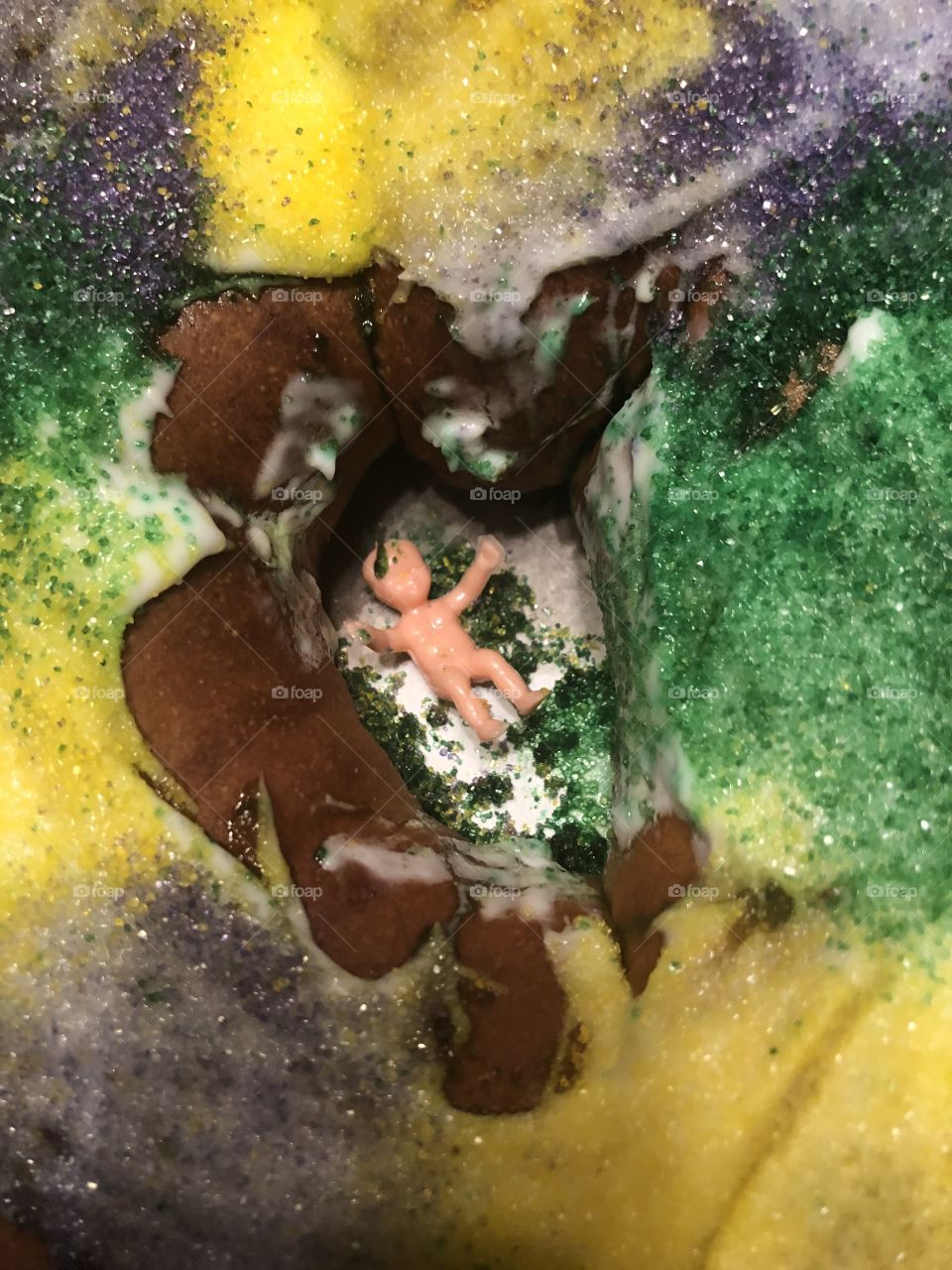 A colorful King Cake made in Louisianna with colorful frostings and sugary goodness, sticking the prize of plastic dollbaby in it. 