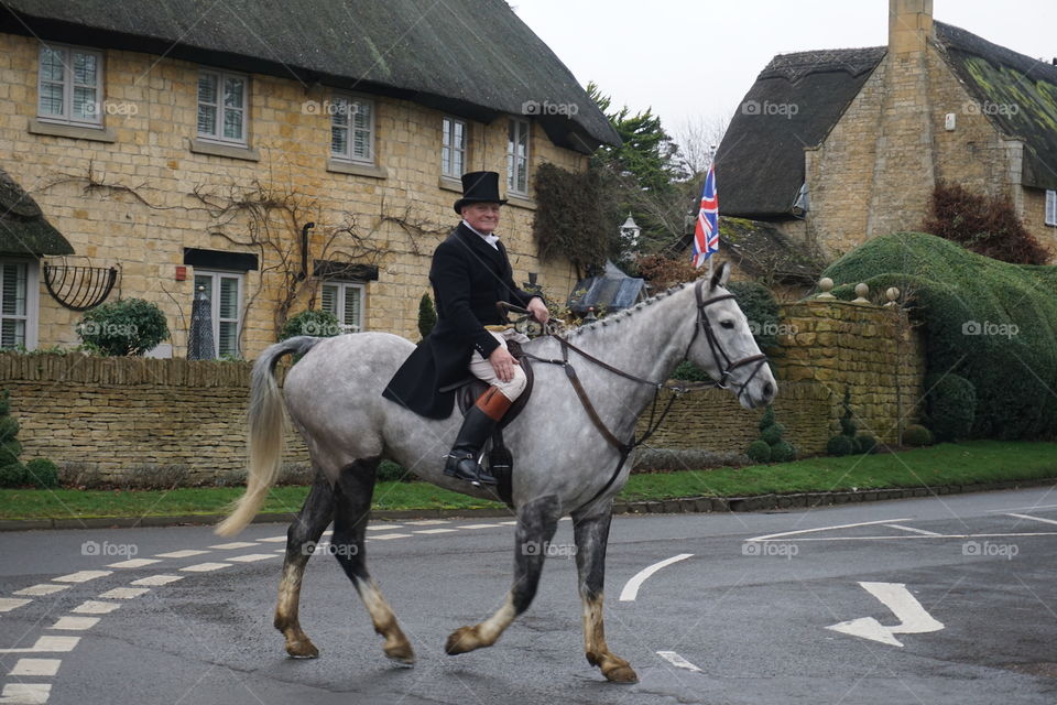 Man riding his dapple grey horse through a Cotswold Village 