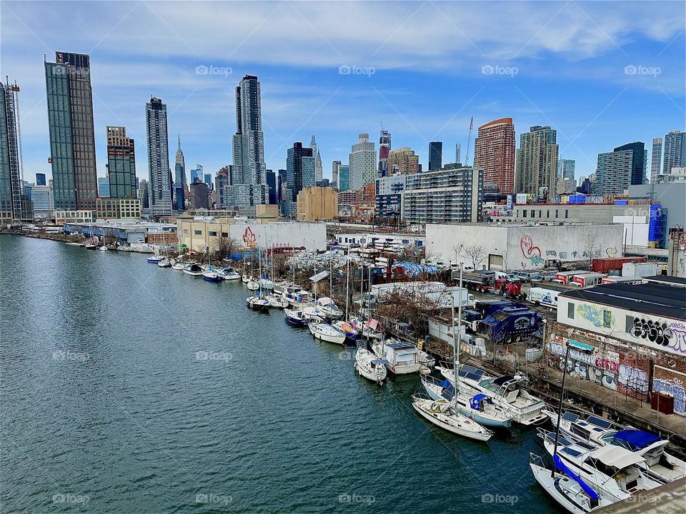 This is „Newtown Creek“ with its many different kinds of boats seen from the „Pulaski Bridge“ that connects „Greenpoint“, Brooklyn to LIC, Queens. Across the waters of the „East River“ we see „Manhattan“. 2024. Hypnotic Productions