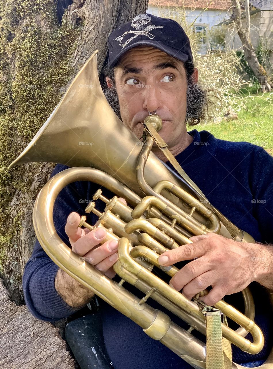 Portrait of Ricardo under a tree playing his tuba 