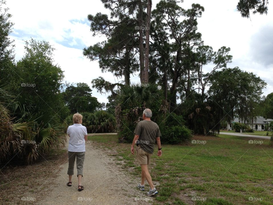 Adult mother and son walking down a dirt road surrounded by trees.