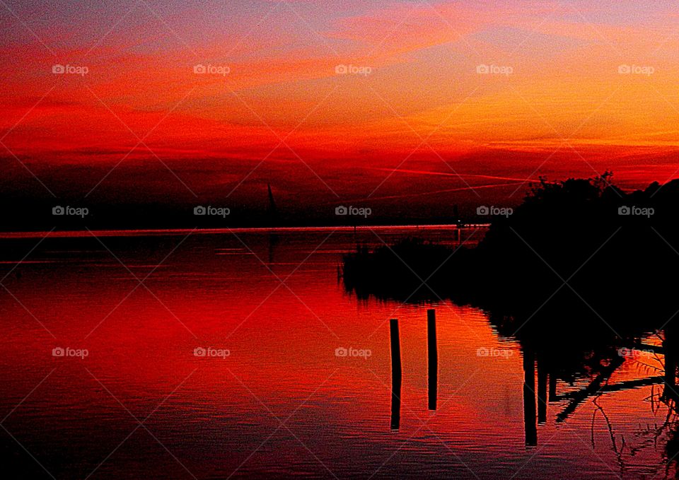 Crimson Beauty - the colorful results of the descending sunset as it cascades its glorious colors across the waters surface. The dock is reflecting on the water surface as well is the tree line.