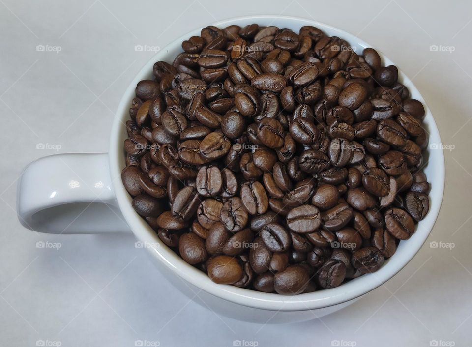 ceramic cup full of roasted coffee beans