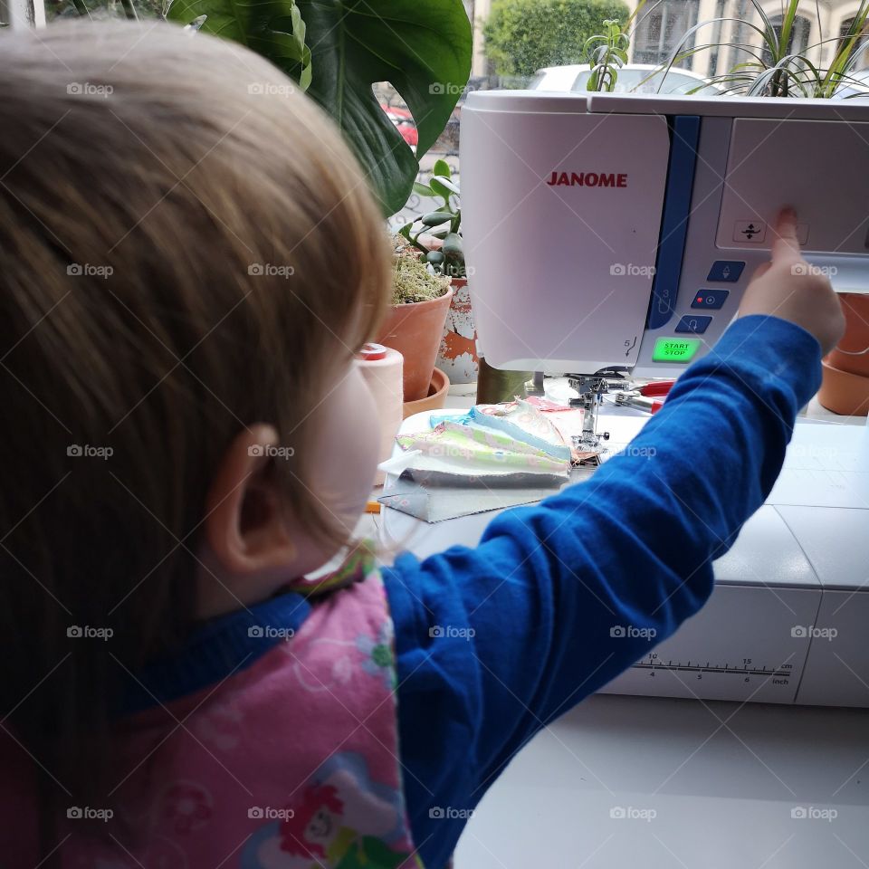 young girl pushes the button on the sewing machine with plants in the background including a monstera