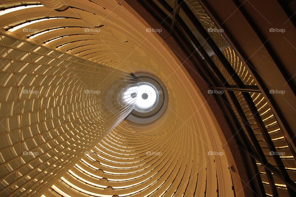 A portrait of the inside of an eliptical skyscraper building. its floors are eliptically shaped and they end in a circle at the top.