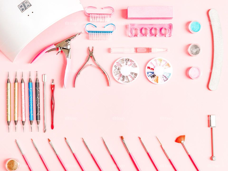 Set for nail master consisting of nail drying lamp,scissors,brushes,nail polish,nail file,rhinestones copy space in the center on a soft pink background,flat lay, close-up. The concept of cosmetics and beauty salons.