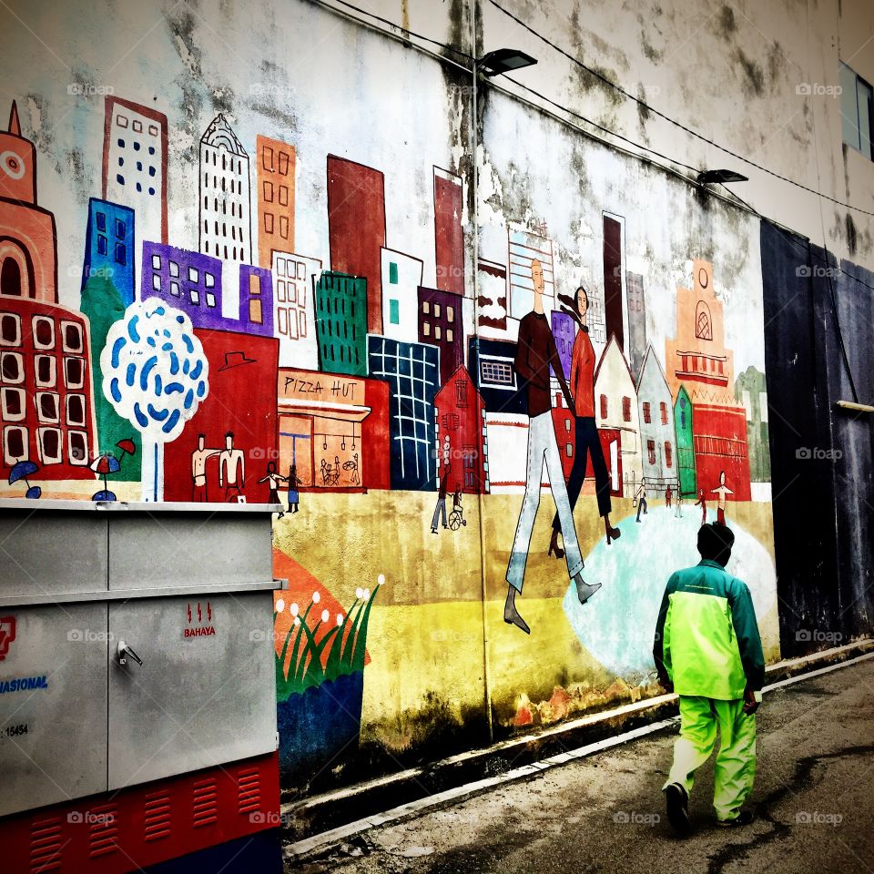 Man in uniform walking past a wall filled with paintings and murals, with a electrical panel from tananga nasional, Malaysia 
