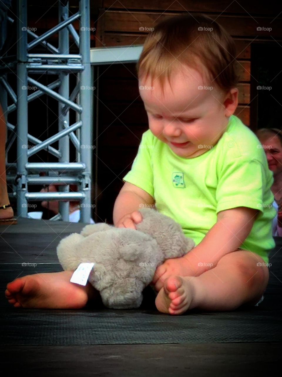 Small children.  A little boy in a diaper is sitting on the stage with his favorite toy.  Boy smiling at his toy