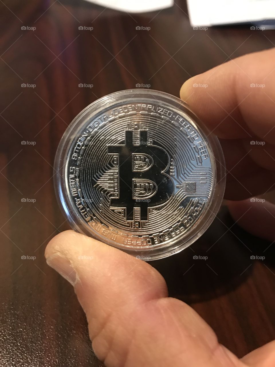 Fingers holding a shiny silver bitcoin 
