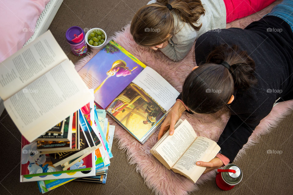 Mom and daughter reading together. Staying mentally in shape starts with good habits from a young age. Stack of books to show love for reading and knowledge. Photo from above. Healthy snacks on the side for a healthy lifestyle.